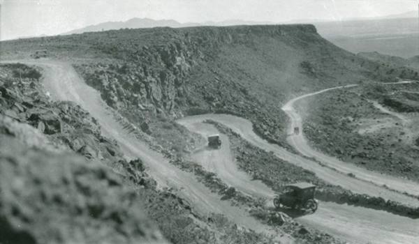 black and white 1920s cars driving down a zig-zag hairpin turns downhill road at La Bajada Hill