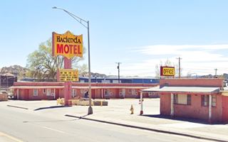 color. Pinkish color single story u-layout motel with yellow-red neon sign in central courtyard seen from US66