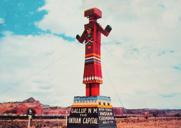 large roadside Kachina doll sign by US66, red rock mountains beyond
