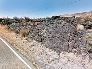 wall of solid black lava beside highway shoulder, highway seen lower left