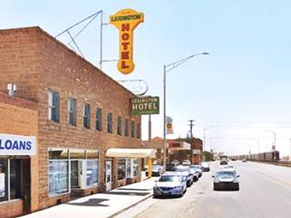 stone faced 2 story building, street to the right, two neon signs on the building, LEXINGTON HOTEL in yellow and red, vertical sign, below green and white box shaped one