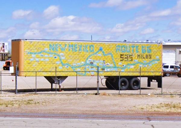 semi-trailer parked by US66, covered in yellow license plates with green and black ones marking US66 alignment and towns across New Mexico