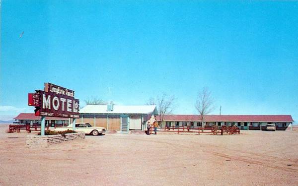 motel units parallel to highway behind an office, gravel driveway, motel red and white sign. All seen from US66 color 1960s postcard