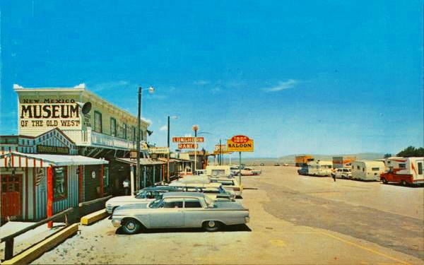 left: cars parked facing fake Far West buildings, neon signs, Route 66 running across the page top to bottom in a color 1960s postcard