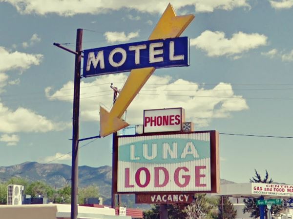 vintage neon sign word MOTEL in white letters accross a blue rectangle and a yellow arrow slanting down. Below another sign saying PHONES-LUNA-LODGE-NO VACANCY