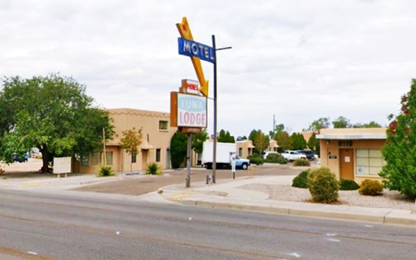 Pueblo style motel, neon sign with yellow arrow seen from Rte 66. U-shaped layout, two story bldg. on the left sign on the right