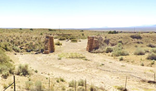 color, stone abutements of a bridge with viaduct, across a dry creek in a desert area with shrubs, mountians in the distance