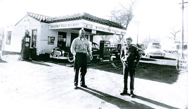 black and white gas station, two men, 1950s cars tiled roof and canopy, gas pumps