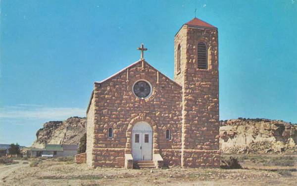 color 1950s postcard of a roughly hewn stone church with steeple on the right, cliffs behind, simple and austere