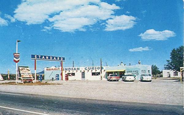 1950s color postcard, single floor, flat roof building, gravel drive, Standard gas sign with blue background and white letters. Cars. Name painted on building, seen from US66