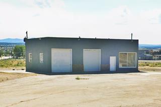 former Mobil filling station Milan NM color view ice-box shaped former gas station building with corner office right, 2 service bays left, no canopy, pumps or pump islands, only a concrete drive