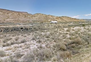US66 in McCartys hills and mesas to the left, black rocks and dry bushes. Freeway beyond and Route 66 to the right