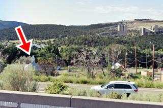 church to the left (red arrow marks it), car, on highway, trees, wooded hills and cement factory in the distance