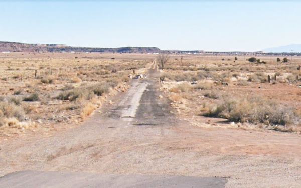 old potted highway runs into the distance in an arid shrub grown scenery. Trucks on I-40 can be seen ahead