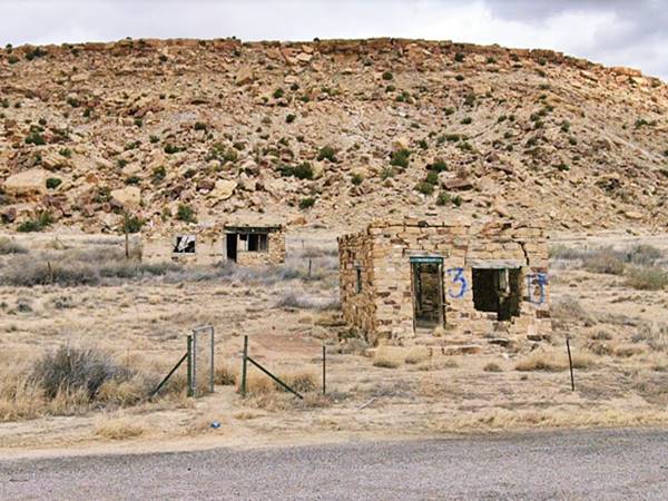 vacant ruins of stone buildings, empty door and windows seen from US66, mesa behind