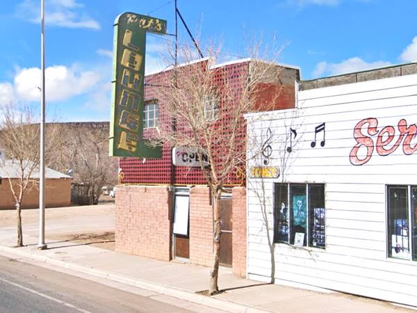 color view, 2 story bar, with green neon sign with yellow letters over sidewalk, Route 66 runs in front of it