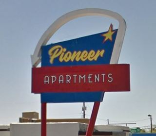modernized neon sign with word PIONEER and a star in yellow on a blue trapezoid and the word APARTMENTS in white on a red rectangle below it. A white arrow curves over the upper part and points down
