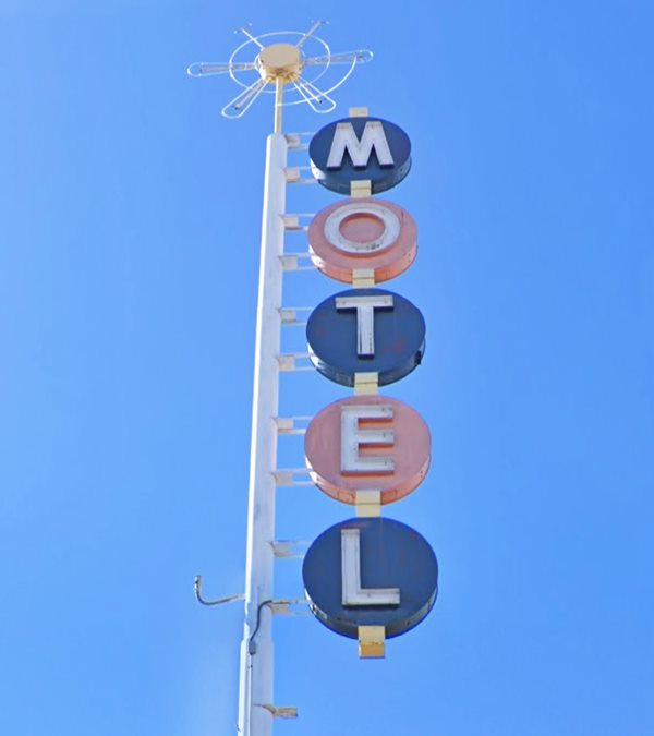 1950s motel neon sign formed by circles alternating in blue and pink color, with the letters M, O, T, E, and L in each of them, fixed vertically along a white steel pole topped by a star