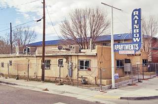 corner ochre single story Pueblo style motel with blue and white neon sign RAINBOW Apts facing Route 66