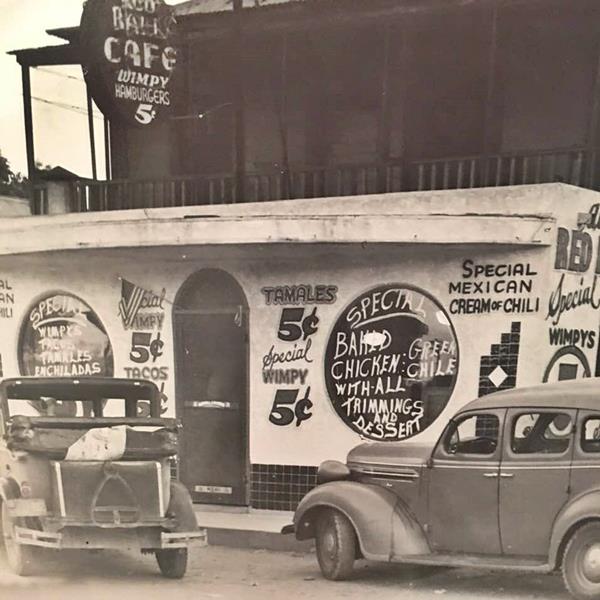 black and white image Red Ball cafe facade, round windows, signs painted with meal prices, a 1930s picture. Cars parked by the cafe