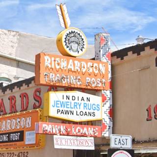orange, with white letters, and several sections, a classic 1950s neon sign of a trading post, also whiute with blue and black letters, red with white, an arrow and an Indian head with headgear