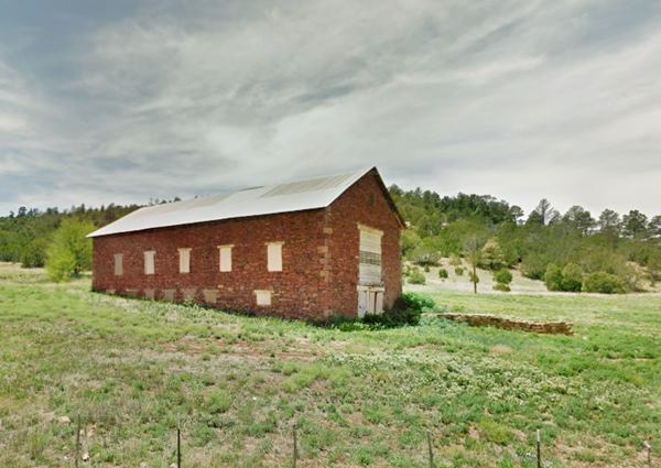 color view stone building a barn, gable roof, in a meadow, trees on hill beyond