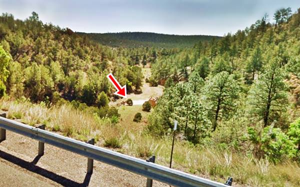concrete bridge deck in a valley surrounded by wooded hills marked with a red arrow seen from the freeway