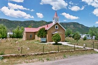 Rowe Catholic church gable roof, single steeple, hills beyond, cemetery to the left, a church.