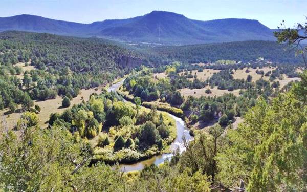 Pecos river meanders across a forested valley with meadows, wooded hills on both sides and in the distance