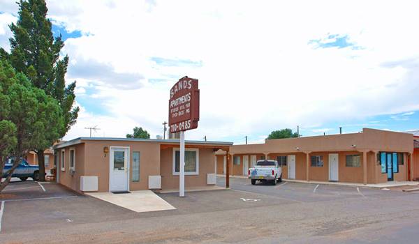 block shaped buildings, painted beige, cypress trees left, pick up truck parked