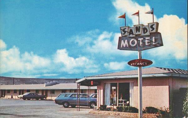 color late 1960s postcard showing a motel office, cars units behind, and a neon sign reading SANDS MOTEL