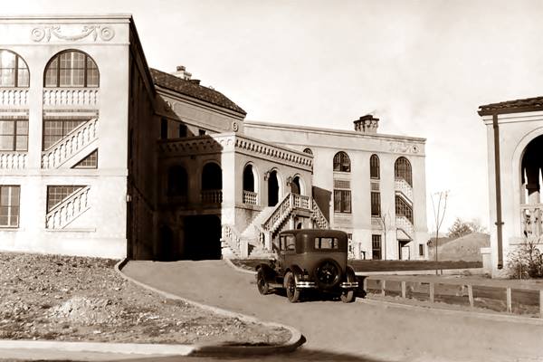 Santa Fe Hospital ABQ in the 1920s sepia photo of 3 story building, mansion-like, with windows and a car driving up its drive c.1920s