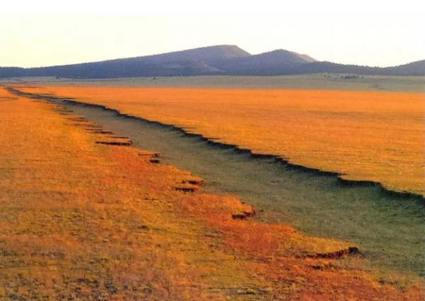 rut cut into the flat plain with reddish grass, hills in the distance