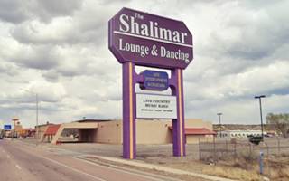 block building, with canopy and violet signpost, vacant, US66 to the left