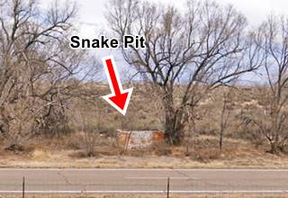 Brown box-shaped concrete snake pit trees and shrubs around it, US66 passing in front of it