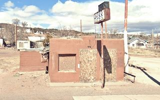 2021 view Star Cafe US66 Grants, New Mexico square brown building with boarded windows on each side of a boarded door. Pueblo style, sign in front. Hill beyond