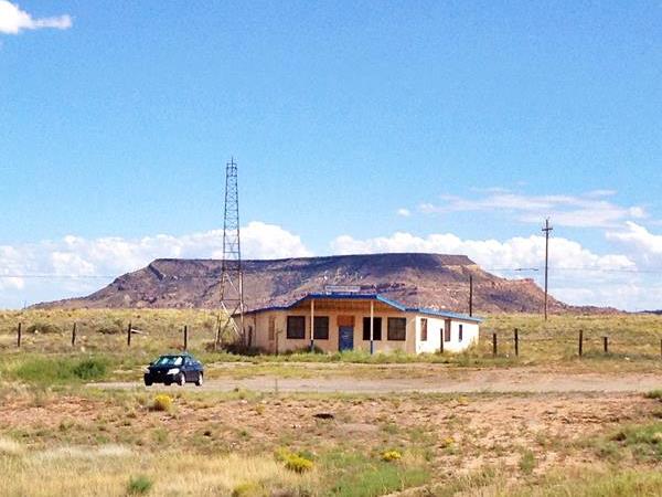 Old Bar next to Route 66 in an arid setting. Car parked, tower to the left, hills in the distance