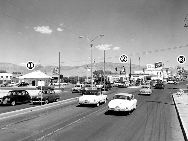 black and white view junction of Central Ave -right- and Monte Vista Blvd. -left, Girard runs across the image. Cars, bar, gas station, theater and restaurant. Sandia mountains in the distance in the mid 1950s