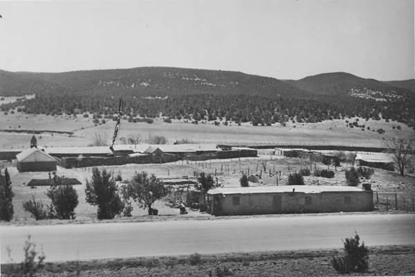 black and white picture, US 66 runs across the image. Behind, fields, trees, a building facing highway and, left, church with steeple
