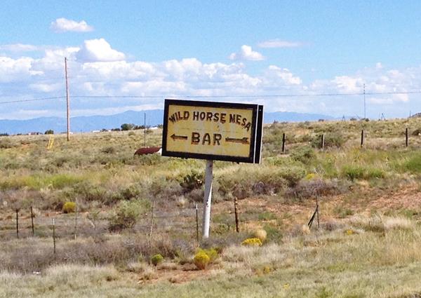 sign pointing to an old Bar next to Route 66 in an arid setting