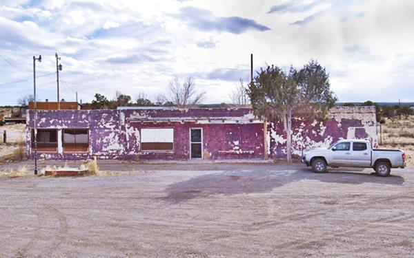 single story stucco flat roof building, gas pump island left, pick up truck right. Tree. Former Trading post on Route 66, New Mexico