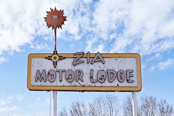 1950s motel sign words: ZIA MOTOR LODGE written on it, star-shaped decoration on the upper tip of a slender pole on the left side of the rectangular white and yellow sign