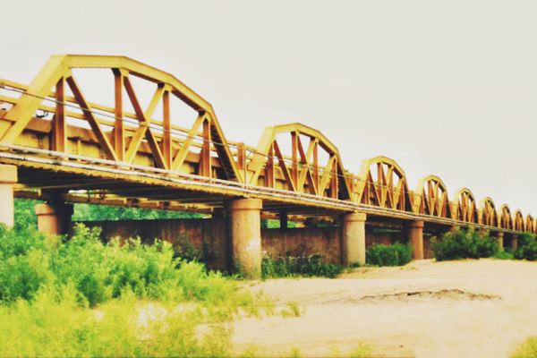 several yellow steel arches of the bridge, seen from the sandy river bed