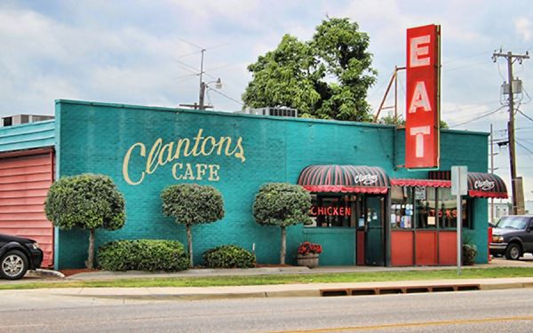 Large red sign with word EAT written on it and green building: Clanton’s Cafe on US66 Vinita