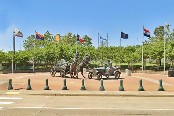 East Meets West statue Tulsa Route 66 bronze sculpture with the 8 Route 66 states flags behind. Cart with bolting horses meets Ford car with people in it