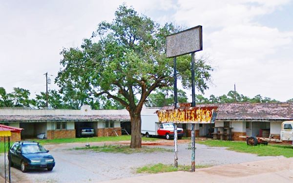 old motel with rusty neon sign and tree