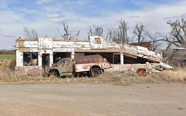 old gas station with roof caving in and rusty truck in front of it