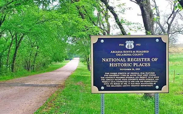 Route 66 runs under the cover of green trees, marker on shoulder