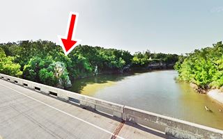 forest and rock cliff over river, seen from bridge.