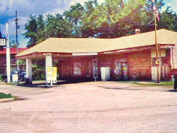 gable roof canopy over pumps island, brick building, a 1980s photo of the DX gas station